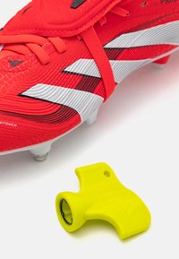 Red soccer cleat with textured surface and white stripe detailing, alongside a bright yellow accessory with a circular opening.