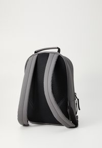 Mochila gris con respaldo de malla acolchada y transpirable, correas ajustables y cuerpo de textura suave. Incluye un asa en la parte superior para transportarla.