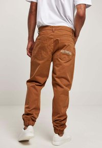 Brune cargo-bukser med elastiske manchetter, to baglommer med hvid "SOUTHPOLL ORIGINAL" tekst, lavet af holdbart materiale. Båret med hvide sneakers.