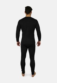 Schwarzes langärmliges Thermooberteil und enge Hosen aus strukturiertem Stoff, mit engen Bündchen und klassischem Design, von hinten betrachtet.