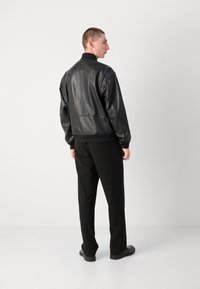 Zwarte leren bomberjack met een hoge kraag, gestructureerde afwerking en geribde manchetten. Slim-fit zwarte broek en zwarte schoenen worden gedragen.