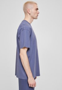 Tricou din bumbac mov, de mari dimensiuni, cu mâneci scurte, guler rotund și o croială lejeră. Textură netedă, design minimal, fără modele sau accente.