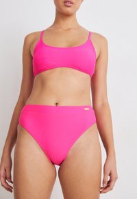 Conjunto de bikini rosa com um top de decote arredondado, alças finas e parte de baixo de cintura alta. Feito de material liso e elástico com detalhes de marca discretos.