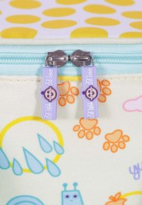 Zwei lila Reißverschlussanhänger mit lächelnden Babygesichtern und dem Text "Milch..." auf einem bunten Stoffbeutel mit Regentropfen- und Pfotenabdruckmustern.