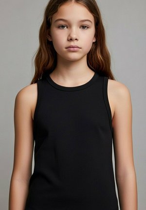 Ragazza con capelli castani lunghi che indossa una canottiera nera, rivolta frontalmente con un'espressione neutra su uno sfondo grigio uniforme.