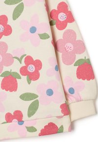 Tessuto a fantasia floreale con fiori rosa, rossi e blu su uno sfondo crema. Polsino e orlo a coste con una finitura morbida e testurizzata.