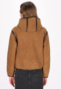 Bruine suedepel met een capuchon, voorzien van donkerbruine accenten langs de naden en manchetten, en een cropped ontwerp bij de taille.