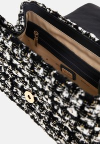 Borsa a tracolla in tweed bianco e nero con hardware dorato, tasca con zip e interno beige. Presenta un tessuto testurizzato e una chiusura a pulsante sicura.
