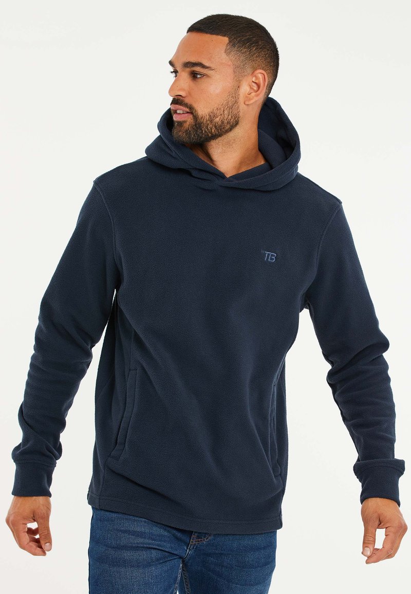 Marineblauwe fleece hoodie met een kangoeroezak, geribbelde boorden en een subtiel logo op de borst. Zachte textuur en relaxed fit.