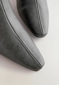 Grå læder ankelstøvler med spidse tæer og tekstureret overflade. Har synlige syninger langs sømmene. Glat, strømlinet design.