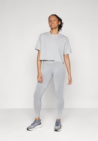 Camiseta gris ajustada de manga corta combinada con leggins grises ajustados que presentan patrones texturizados. La modelo lleva zapatillas deportivas grises.