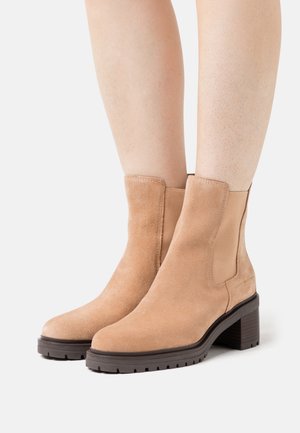 Bottines en daim beige avec des panneaux latéraux élastiques, un bout rond et un talon bloc empilé, dotées d'une semelle en caoutchouc texturé.