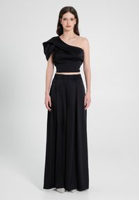 Completo nera a due pezzi composto da un top cropped con spalla scoperta e manica a sbuffo drappeggiata, abbinato a pantaloni a gamba larga plissettati a vita alta.