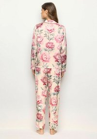 Set de pijama floral, cu mâneci lungi și pantaloni. Material moale, cu un fundal crem și modele de bujori roz. Croială lejeră, cu guler.