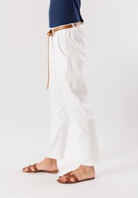 Pantaloni bianchi, morbidi e svasati con vita alta e tasche laterali, abbinati a sandali piatti marroni con un design a fibbia.