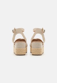 Beige kilklackssandaler med övre i tyg, justerbara vristremmar och plattform av naturliga fibrer. Dämpade innersulor och texturerad gummisulor.