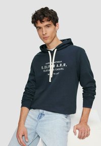 Felpa blu navy con chiusura a coulisse, lettering bianco sul petto, polsini a coste e una vestibilità comoda. Dotata di tasca a marsupio.