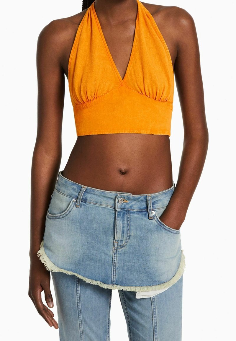Top court orange à dos nu avec un détail froncé, associé à une jupe en jean bleu clair avec un ourlet effiloché et une poche avant.