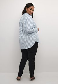 Camisa de botones a rayas azul claro con cuello y mangas largas, combinada con pantalones negros ajustados y sandalias de tacón negro.