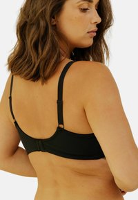 Soutien-gorge noir avec bretelles ajustables, en tissu lisse, fermeture croisée et accents en dentelle le long de la couture inférieure. Vue arrière montrée.
