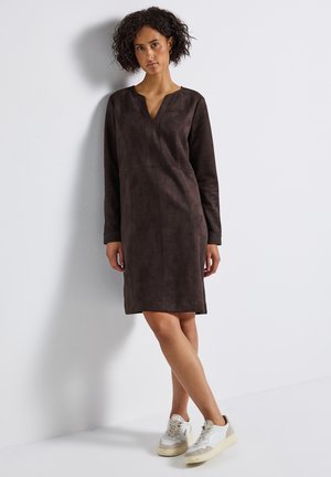 Brown suede dress with long sleeves, V-neck, and seam detailing, falling above the knee. Paired with white and beige sneakers.