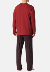 Rotes Langarmhemd kombiniert mit marineblauen gemusterten Hosen mit geometrischem Design. Das Outfit besteht aus weichem, bequemem Stoff.