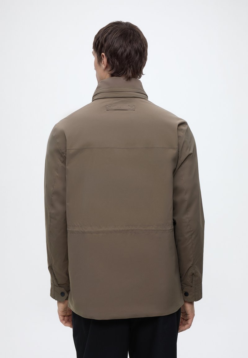 Man wearing a brown long-sleeve jacket with buttoned cuffs, viewed from the back against a plain light background.