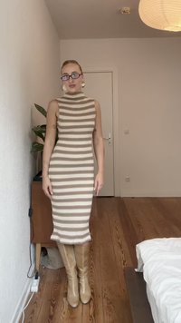Rochie tricotată cu guler înalt și textură nervurată, având dungi orizontale alternante de culoare bej și crem; asortată cu cizme bej până la genunchi.