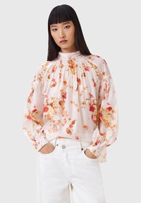 Bloemrijke blouse van lichtroze stof met een geraffineerde halslijn en poffende mouwen, met een multikleurig bloemmotief en elastische manchetten.