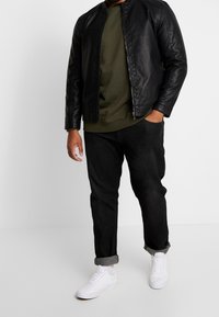 Zwarte leren jack, olijfgroen trui met ronde hals, zwarte jeans en witte sneakers. Opgerolde mouwdetails op de jeans, rits aan de voorkant van het jack.