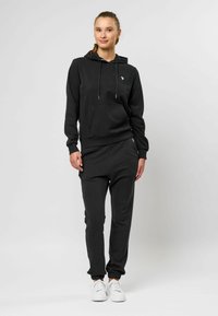 Zwarte hoodie en bijpassende trainingsbroek van zachte stof, met een kangoeroezak, een capuchon met trekkoord en elastische boorden bij de enkels.