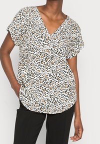 Blusa a maniche corte con scollatura a V in tessuto bianco con motivo leopardato caratterizzato da macchie nere, marroni e arancioni. Vestibilità ampia e orlo arrotondato.