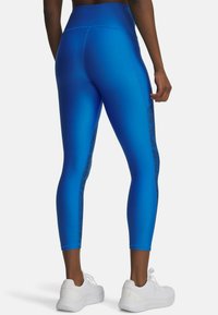 Blue leggings with a textured black side panel, high waistband, and a fitted design, paired with white athletic shoes.