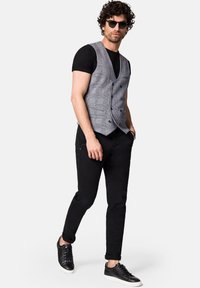 Szary kamizelka w kratę noszona na czarnym t-shircie, czarnych dżinsach i czarnych butach. Posiada podwójne guziki z przodu oraz płaski kołnierz. Podkreślona okularami przeciwsłonecznymi.