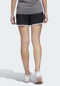 Pantalones cortos atléticos negros con ribete blanco, combinados con zapatillas deportivas blancas. Tono de piel visible y textura suave de las piernas.