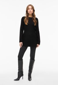 Zwarte gebreide trui met lange mouwen en een rechte pasvorm, gecombineerd met donkere skinny jeans en kniehoge laarzen met een puntige neus. Eenvoudige, minimalistische uitstraling.