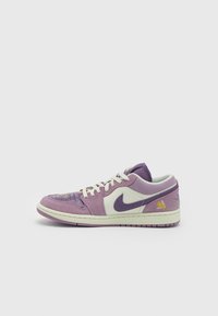 Baskets basses Nike violettes et blanches avec des lacets blancs, un logo Swoosh violet et une petite broderie florale jaune près du talon.
