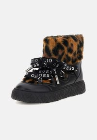 Zapatillas negras de cuero con un puño de piel sintética de leopardo, cordones negros con la marca blanca "GUESS" y suela de goma negra texturizada.