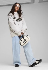 Jasnoszara oversize kurtka z czarnym logo, luźne jasnoniebieskie dżinsy, czarno-bia łe sneakersy oraz biała torebka z czarnymi akcentami.