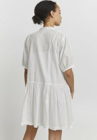 Weißes Baumwollkleid mit einem strukturierten, gepunkteten Muster; kurze Puffärmel; geraffte Taille; ausgestellter Rock mit einem Rüschensaum.