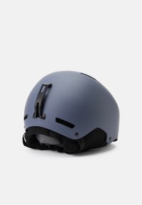 Modrý matný lyžařský helma s větracími otvory, černým polstrováním a nastavitelným páskem. Má zadní klip pro upevnění doplňků.
