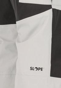 Vedenkestävä takki mustavalkoisen värimaailman kanssa, jossa on geometrisiä värilohkoja, pehmeä kangas ja näkyvä "SLOPE"-logo alhaalla edessä.