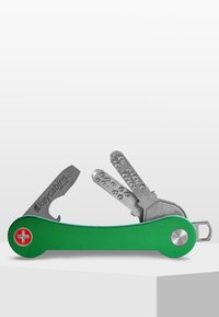 Multiverktygsnyckelorganisatör med grön aluminiumkropp, verktyg i rostfritt stål och en röd schweizisk kors-emblem; har olika nyckelformer och -designer.