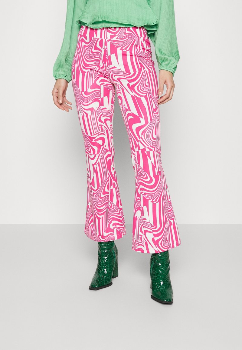 Rozšířené kalhoty s růžovo-bílým vlnkovým vzorem, vyrobené z elastického materiálu. Kombinované s lesklými zelenými vysokými botami.