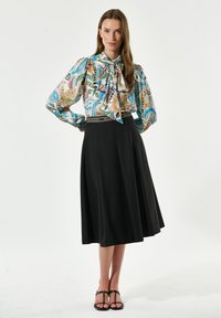 Blus med blommönster och knut vid halsen, tillsammans med en svart A-linjeformad kjol. Svarta sandaletter med remmar fulländar outfiten.