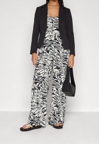 Svart blazer över en jumpsuit med zebramönster i svart och vitt. Bred ben design. En liten svart handväska och platta sandaler fulländar looken.