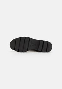 Semelle en caoutchouc noir avec de profondes rainures pour une meilleure adhérence. Présente un embout arrondi et une texture lisse, idéale pour diverses surfaces.