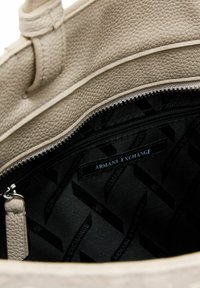 Borsa a tracolla beige con texture, dotata di chiusura con zip e rivestimento interno nero con logo Armani Exchange. All'interno è presente una piccola tasca con zip.