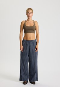 Top corto marrone e pantaloni a gamba larga a righe navy con vita elastica. Tessuto morbido; il modello è in piedi davanti a uno sfondo neutro.