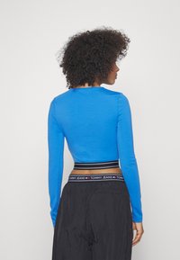 Blå langermet topp med rund halslinje og tettsittende silhuett. Båret med svarte bukser med en merket elastisk midjebånd.